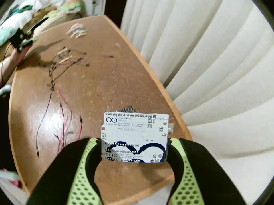 Gripper-camera close-up of a microcontroller board held between the gripper jaws above a desk